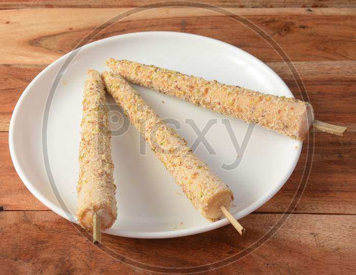 Punjabi Kulfi Is An Indian Traditional Stick Ice Cream, 3 Pieces Of Punjabi Kulfi Served In A White Plate Over A Rustic Wooden Table, Selective Focus