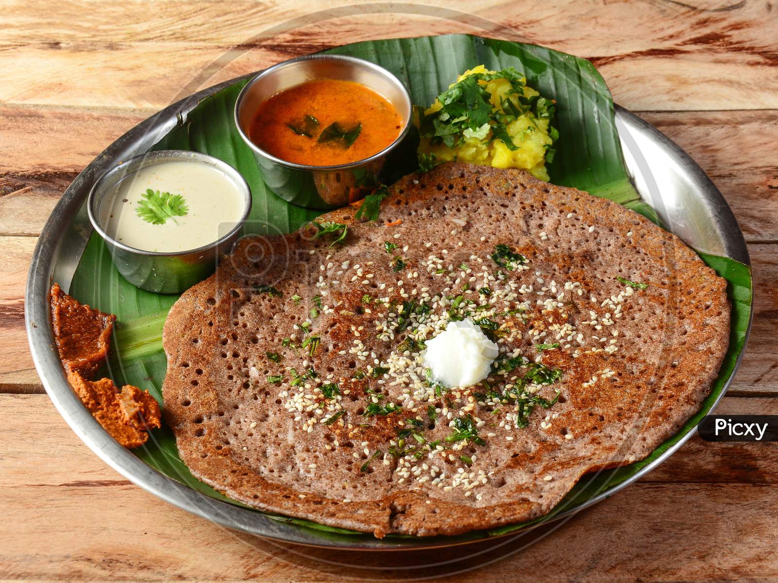 Ragi Dosa Or Finger Millet Dosa A South Indian Traditional Breakfast Served With Chutney,Sambar And Potato Masala Topped With Butter And Served Over A Rustic Wooden Background, Selective Focus
