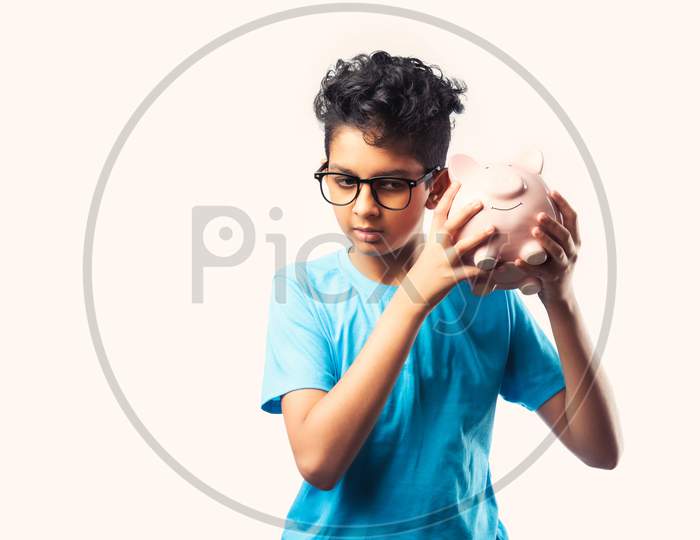 Cute Little Indian Asian Boy Holds Piggy Bank With Books Against White Background