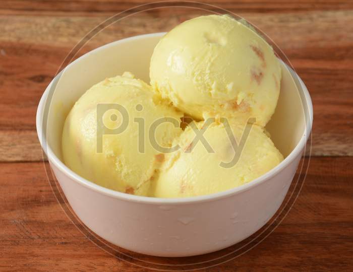 Butter Scotch Ice Cream Scoops Served In A Bowl Over A Rustic Wooden Table, Selective Focus