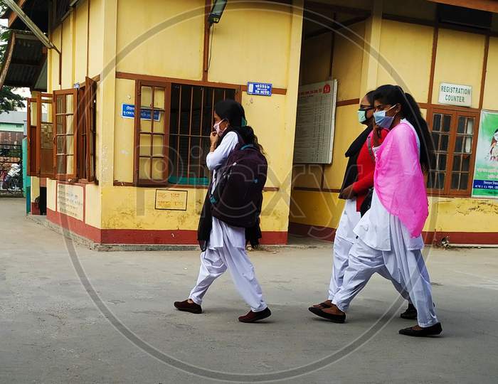 Schoolgirls with backpacks walking in a hospital campus wearing facemasks