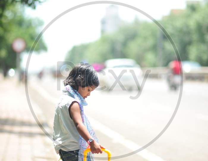 a kid with toy luggage waiting for transport on the side of the road