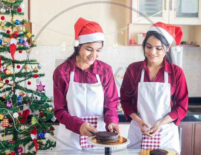 Christmas Preparation And Celebration Concept, Two Young Girls Wearing Apron And Santa Hat Making Cake Bread At Home During Pandemic. Holidays And Festive Season.