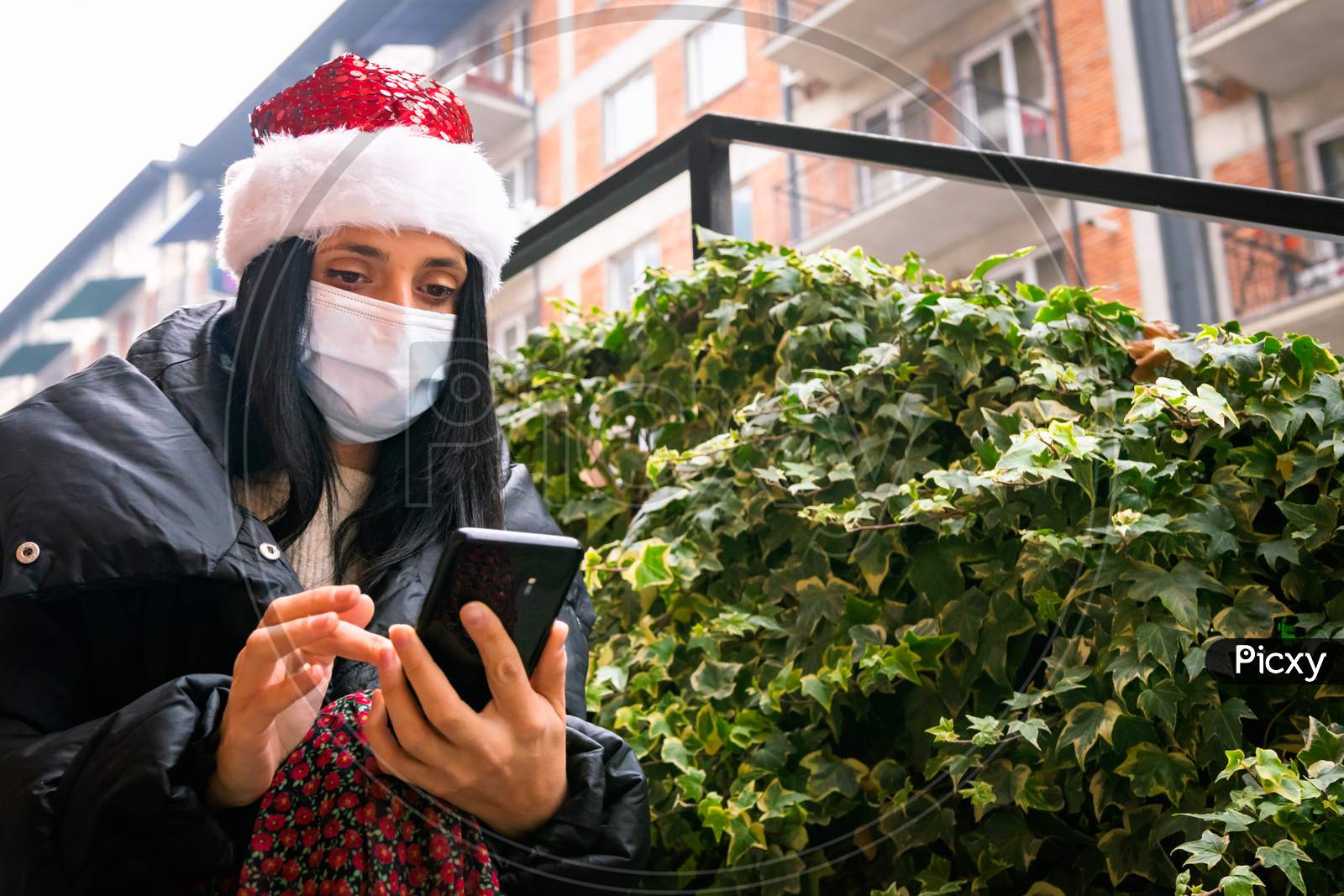 Caucasian Woman With Xmas Hat Texts Outside In The Street. Social Media During Pandemic And Holiday Celebrations And Socail Distancing.