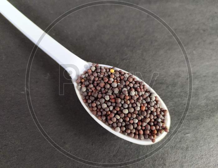 Cooking spice, spoonful mustard seeds on black background.