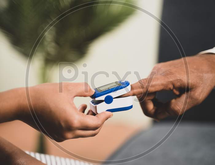 Close Up Of Doctor Hands Checking Temperature Of Old Sick Man Using Infrared Thermometer At Hospital While Both Worn Face Mask Due To Coronavirus Covid-19 Safety Measures.
