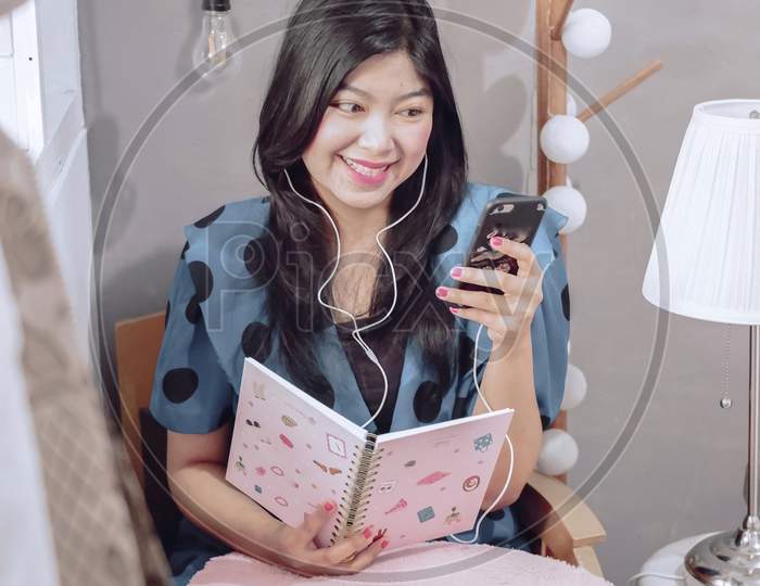 Woman Is Holding A Book While Looking At Her Mobile Phone