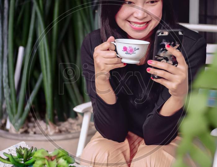 Cute asian girl looking to smartphone in her hand while enjoy the tea