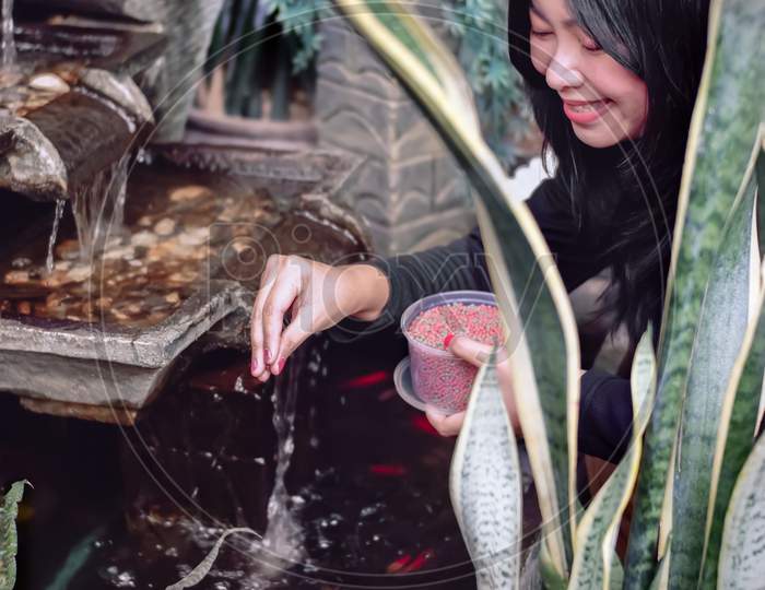 Beautiful asian girl feeding little red fish in the small fish pond