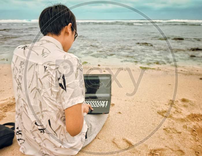 Asian Men Making Money Online Using His Laptop On A Beautiful Beach With A Blue Sky