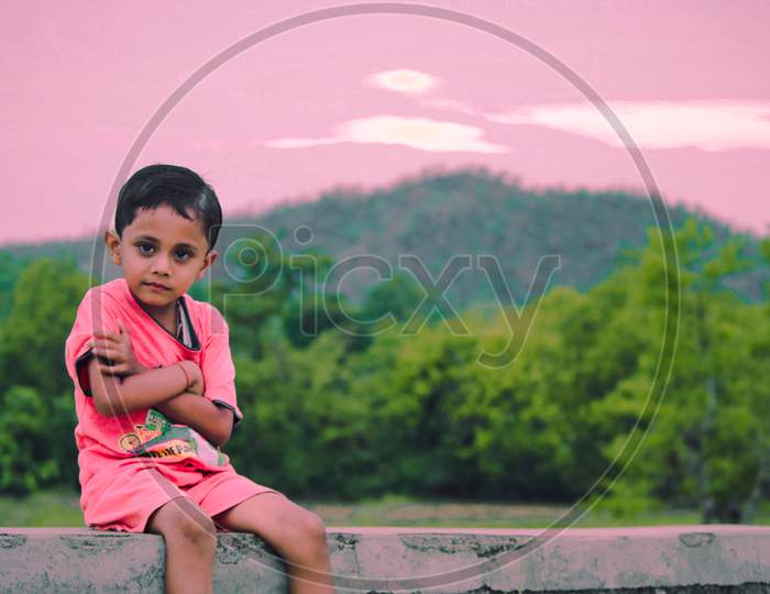 Child sit over pink sky and green nature