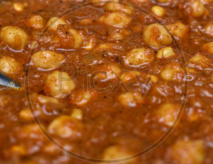 Closeup Shot Of Punjabi Chickpeas Masala Curry Sabji In Round Vessel With Spoon And Black Background .