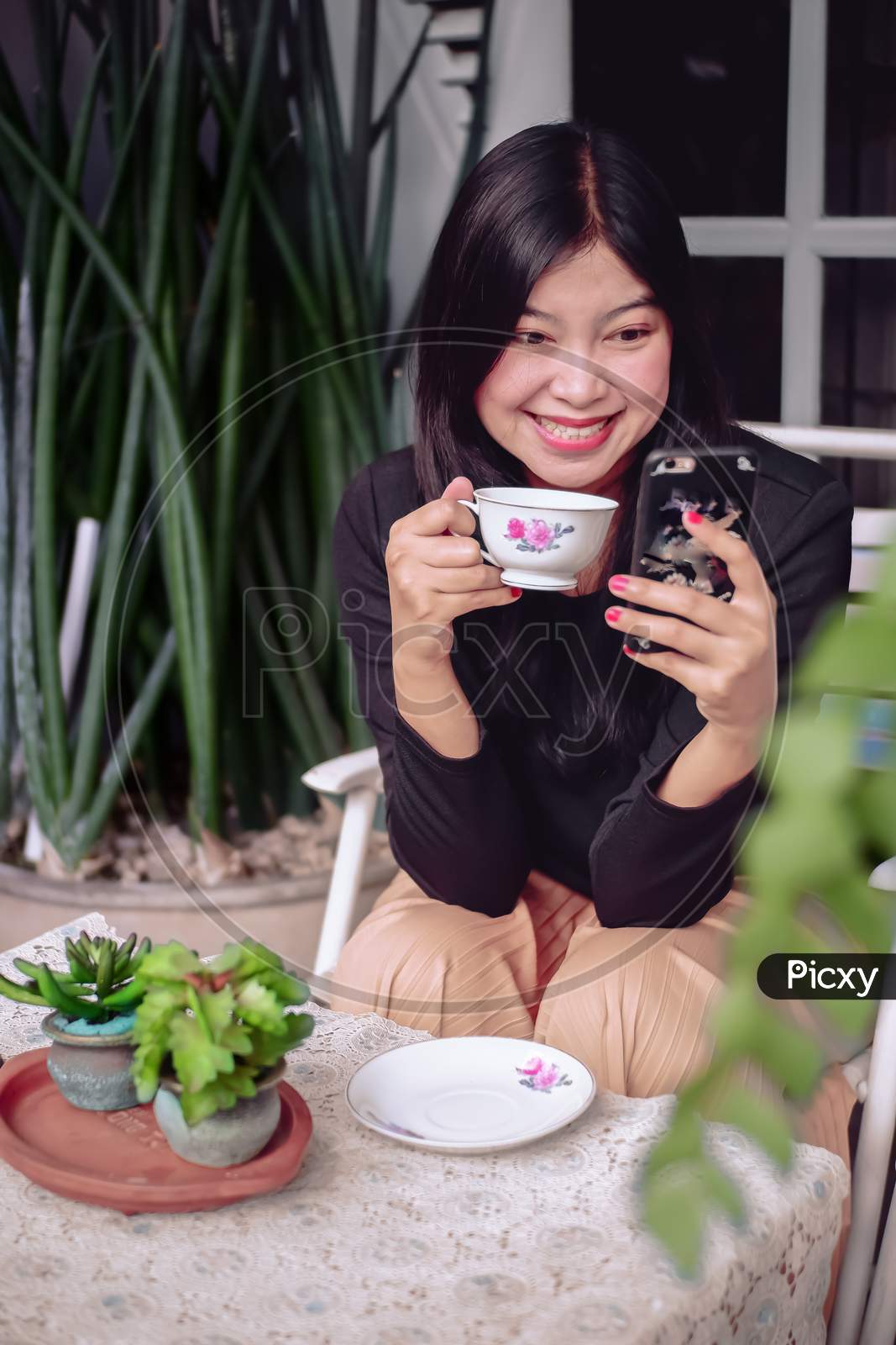 Cute asian girl looking to smartphone in her hand while enjoy the tea