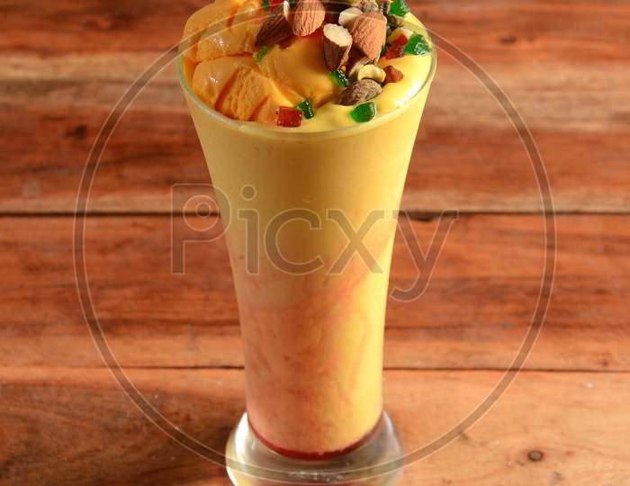 Mango Mastani, Indian Street Food Mango Juice And Ice Cream Blended And Topped With Dry Fruits And Nuts,Served In A Glass Over A Rustic Wooden Background, Selective Focus On Top