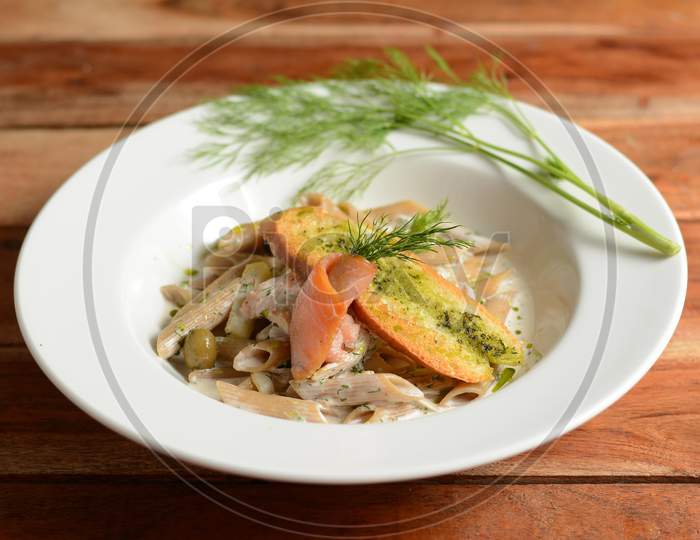 Whole Wheat Penne Pasta With Salmon, Zucchini, Served In A White Plate On A Rustic Wooden Table, Selective Focus