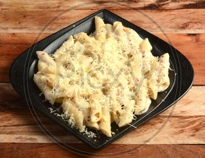 Penne Pasta Topped With A White Creamy Sauce And Basil Served In A Plate On A Rustic Wooden Table, Selective Focus