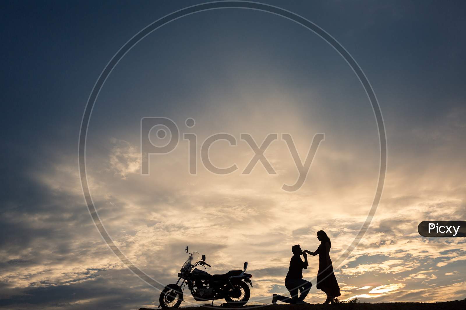 Silhouette of a man kissing his wife hand during sunset
