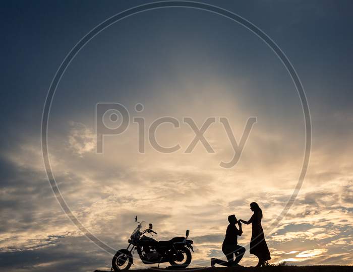 Silhouette of a man kissing his wife hand during sunset