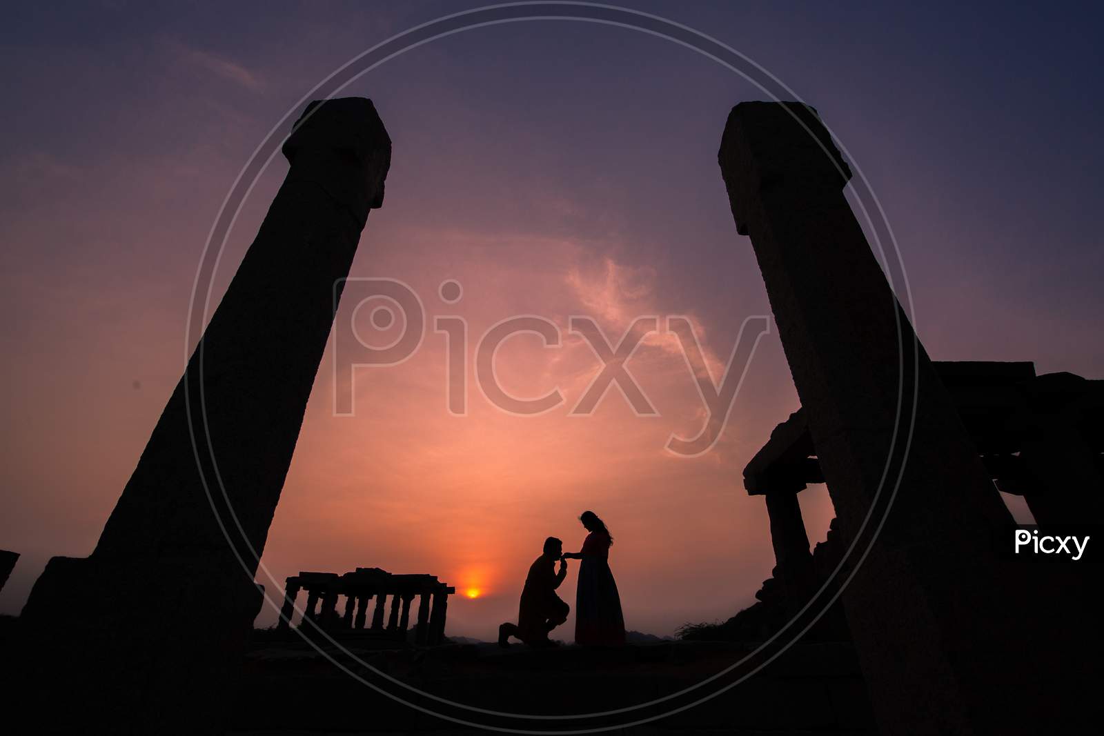 Silhouette of Indian man kissing wife's hand during sunset