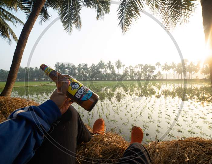 Man Holding a Beer Bottle With Paddy Fields in Background