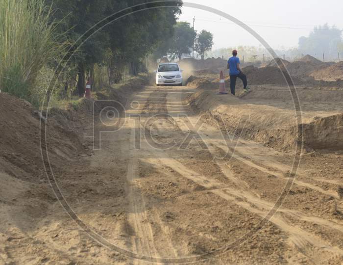 Landscape of a car moving past the man through the dirt road
