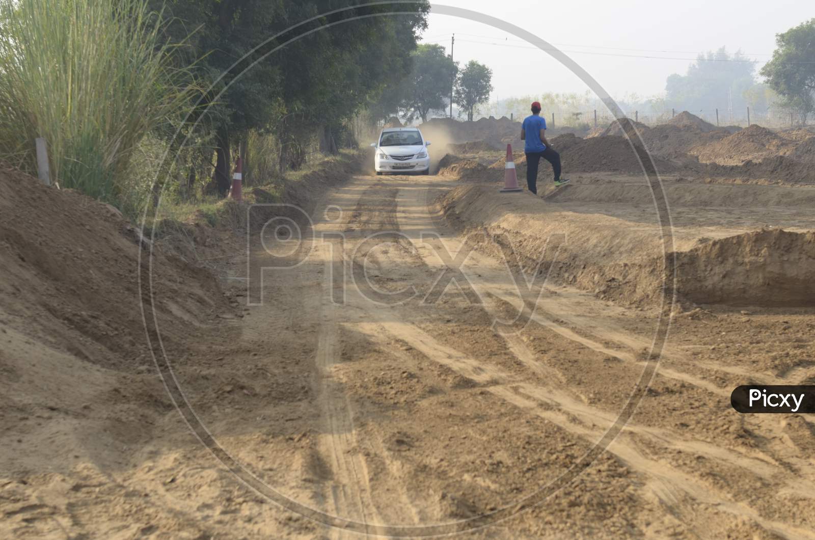 Landscape of a car moving past the man through the dirt road