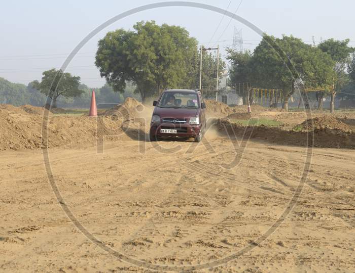 A Red Maruti Suzuki Wagon R Car moving through the dust