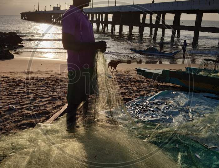 A Fisherman with Fishing Net At A Beach  and Pier in Background  Near Pondicherry  Beach
