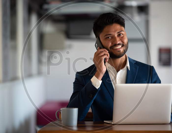 Indian Young Businessman Speaking In Mobile At an Office Desk Background