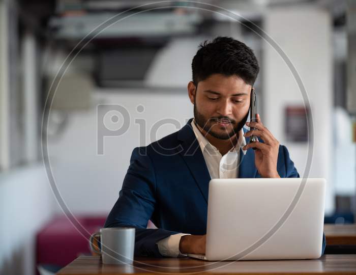 Indian Young Businessman Speaking In Mobile At an Office Desk Background