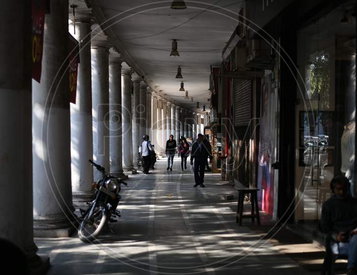 A Shopping Corridor With Pillars And Pedestrians Walking Along The Corridor