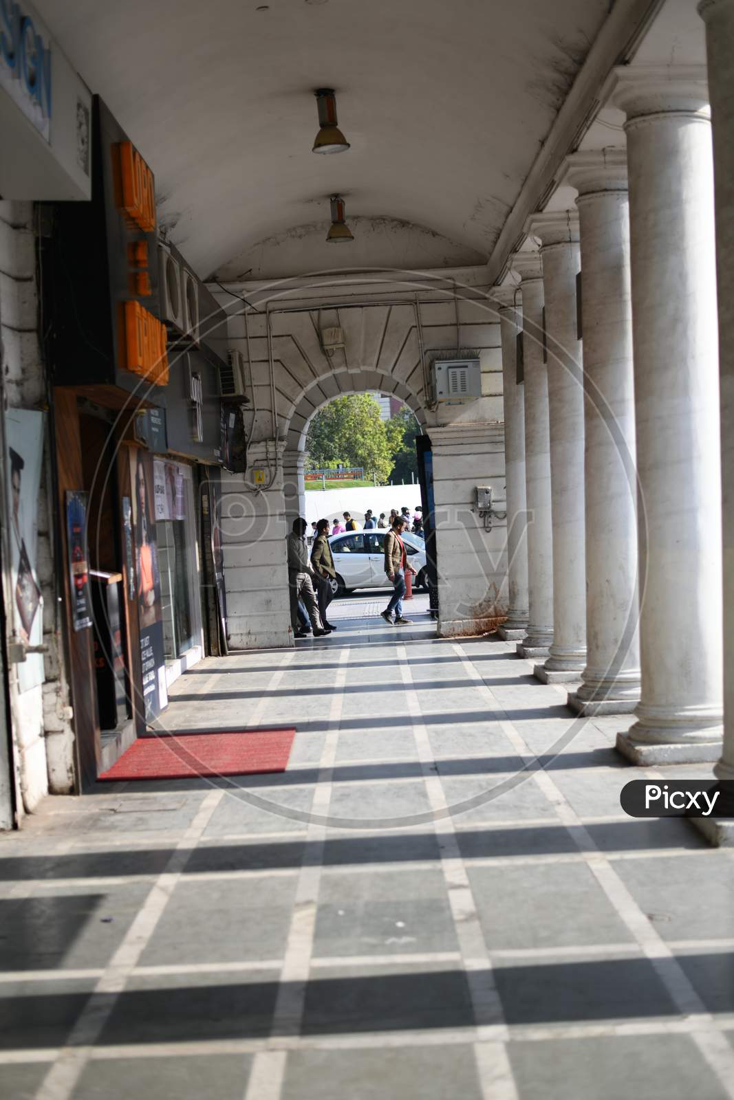A Shopping Corridor With Pillars And Pedestrians Walking Along The Corridor