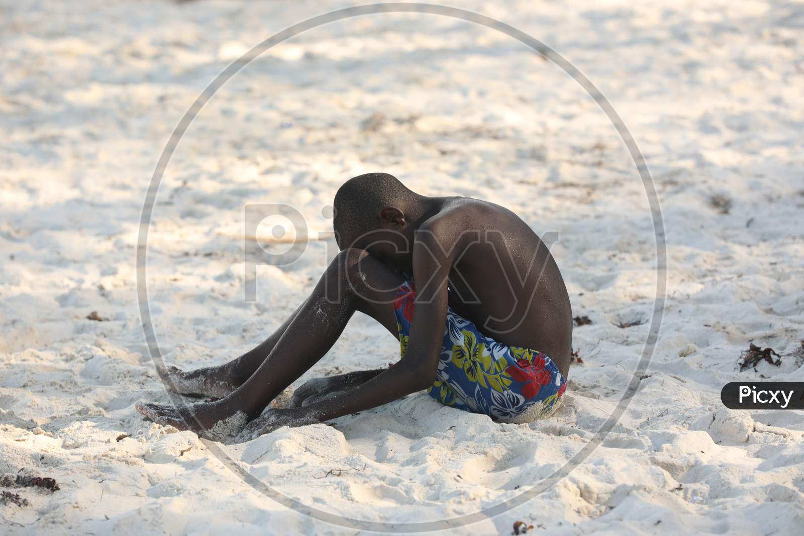 A Shirtless Kenya boy sitting alone by the beach