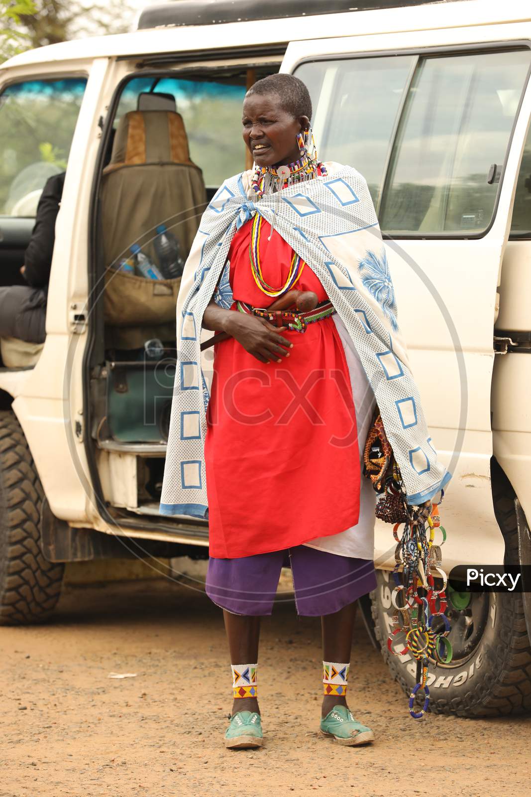 African Tribal woman standing by a car holding handmade accessories