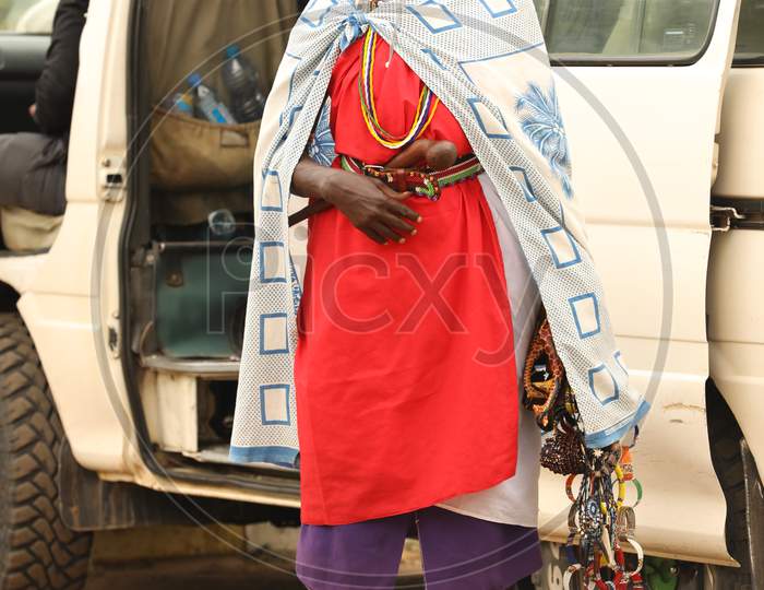 African Tribal woman standing by a car holding handmade accessories