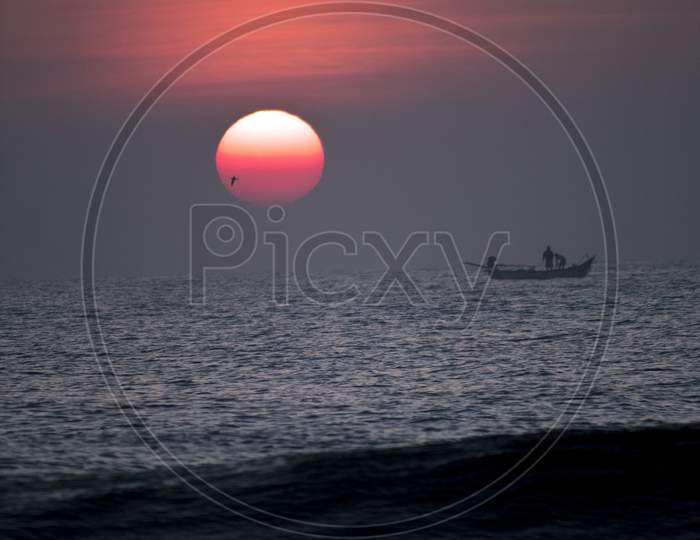 Silhouette Of Fishing Boat On Sea With Sunset Sky  In Background
