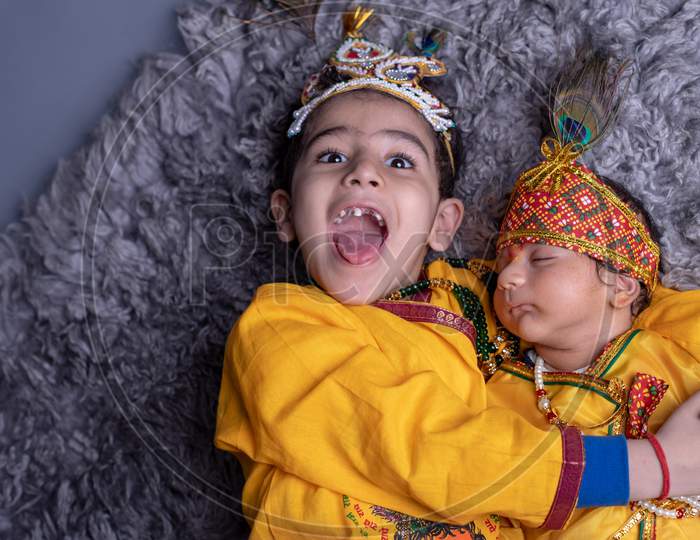Young Indian Brothers Or Siblings Dressed Like Lord Sri Krishna And Posing Over A Gray Background