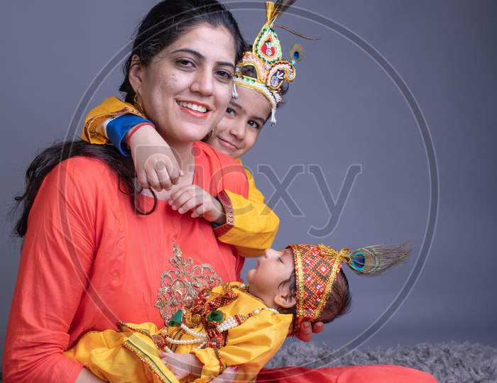 Indian Mother With her Children Dressed Like Lord Sri Krishna And Posing Over a Gray Background