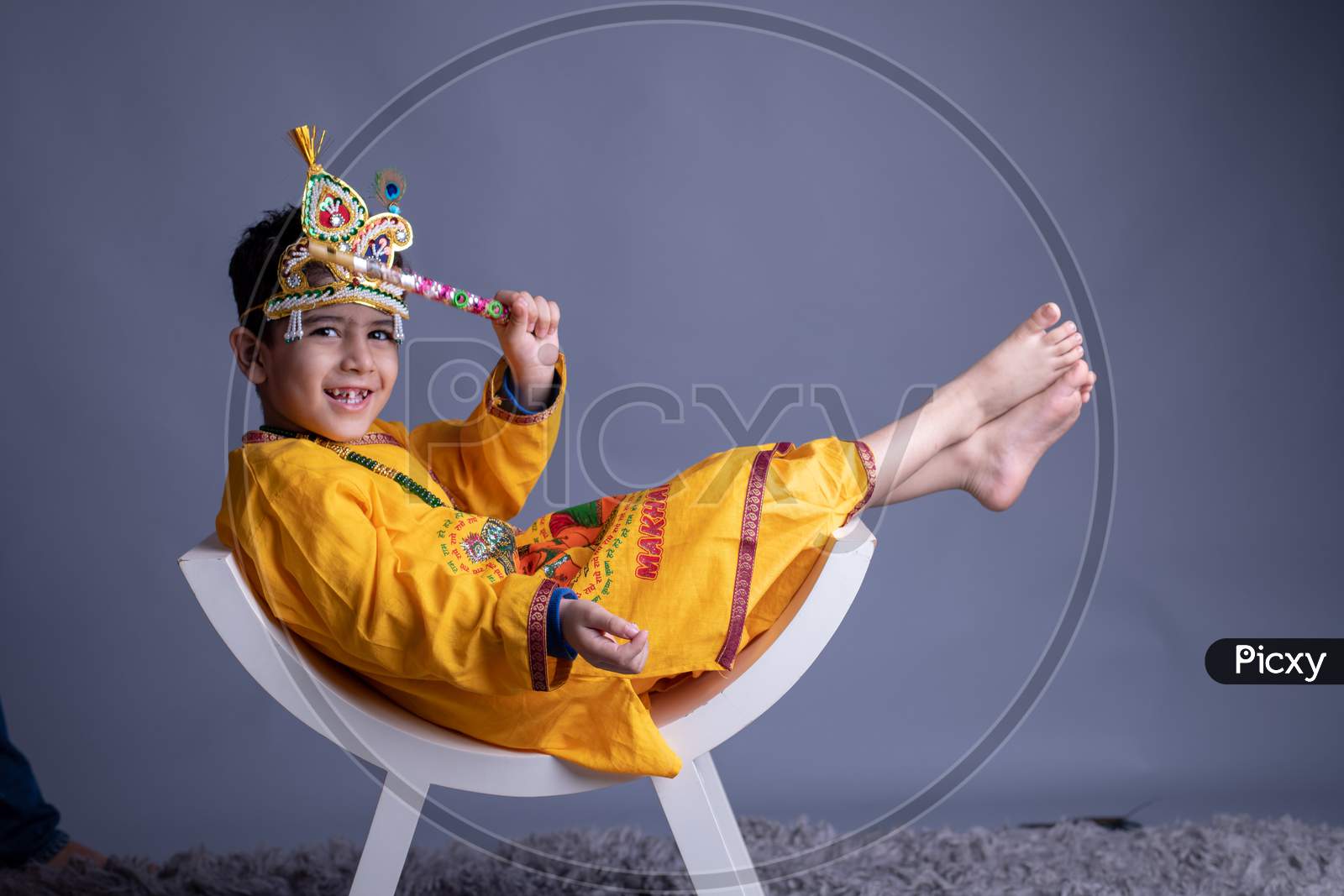 Young Indian Boy Dressed like Lord Sri Krishna And Posing Over an Gray Background