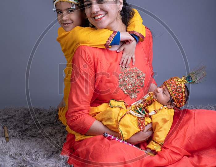 Indian Mother With her Children Dressed Like Lord Sri Krishna And Posing Over a Gray Background
