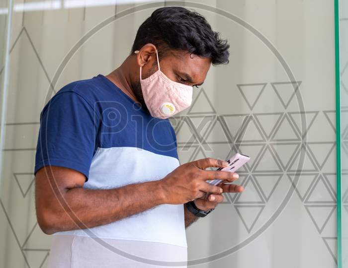 A person using his phone and wearing a mask to protect himself from Novel Corona Virus Covid-19