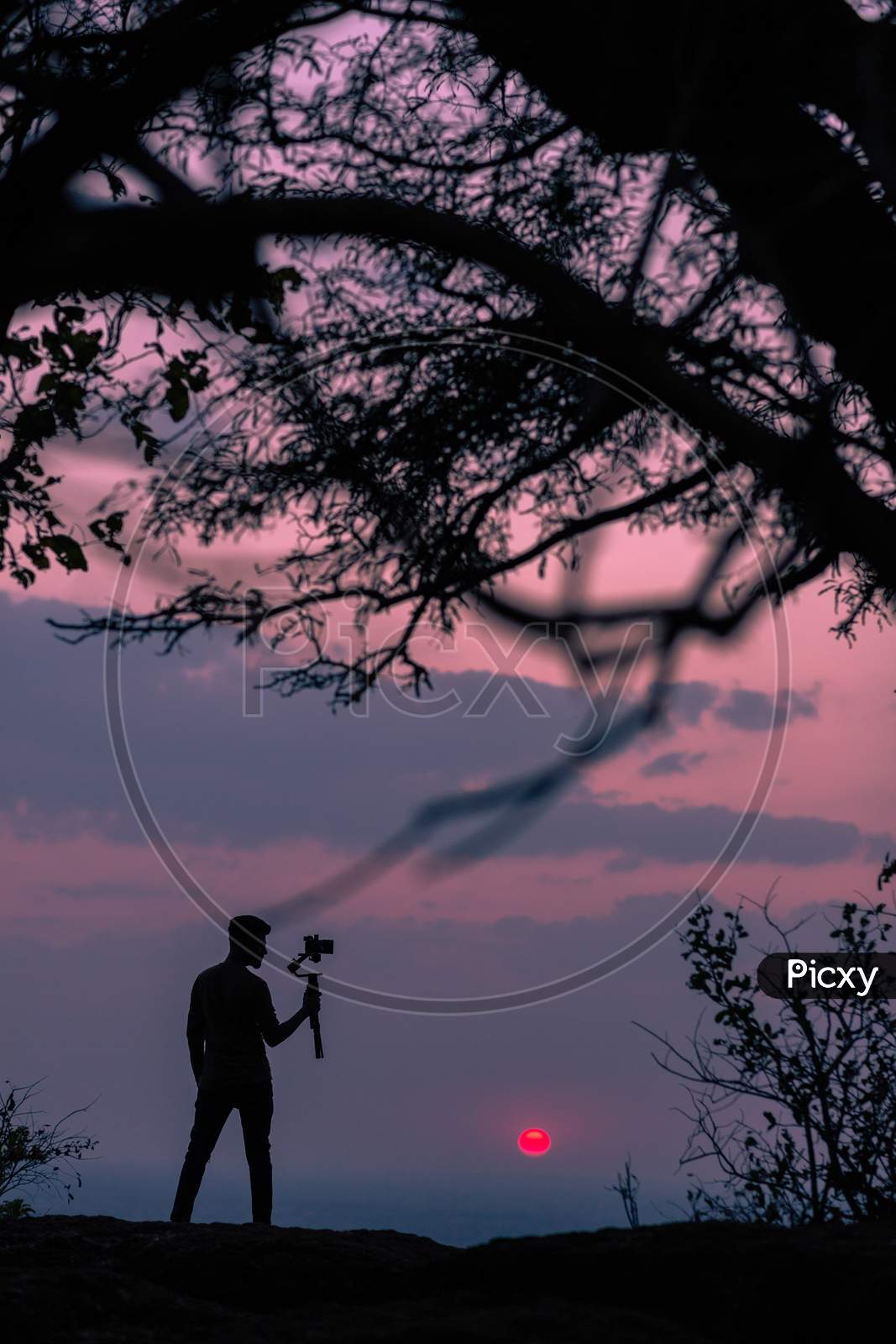 Silhouette Of A Photographer Holding a Camera Over Sunset Sky In Background