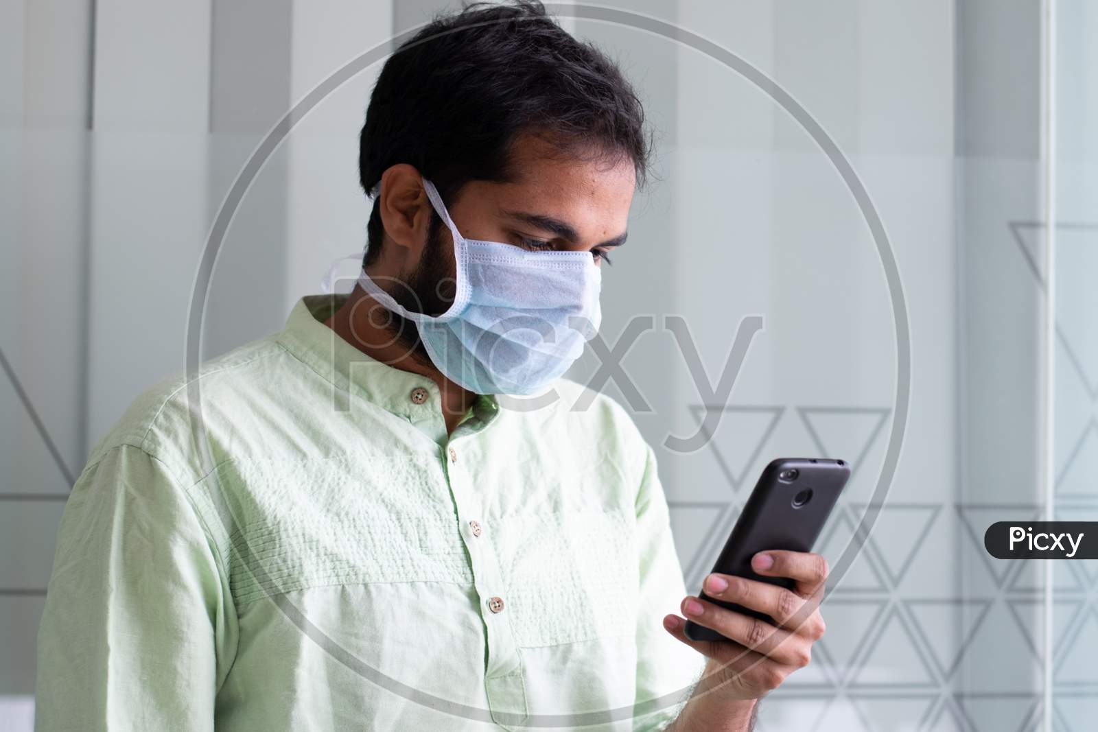 An Indian man wearing safety mask and using smartphone at a office work space amidst of Corona virus outbreak in India
