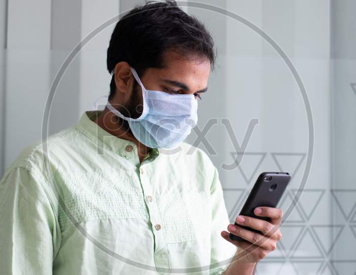 An Indian man wearing safety mask and using smartphone at a office work space amidst of Corona virus outbreak in India