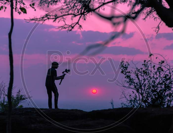 Silhouette Of a Photographer Holding a Camera Attached To Gimbal Over Sunset Sky In Background