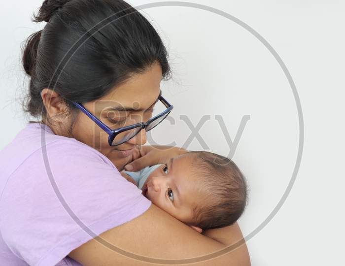 A Young Mother In Spectacles Looking At Her Infant Baby Boy In Her Lap In Solid Grey Background With Space For Text. Mothers Day Concept Photo.