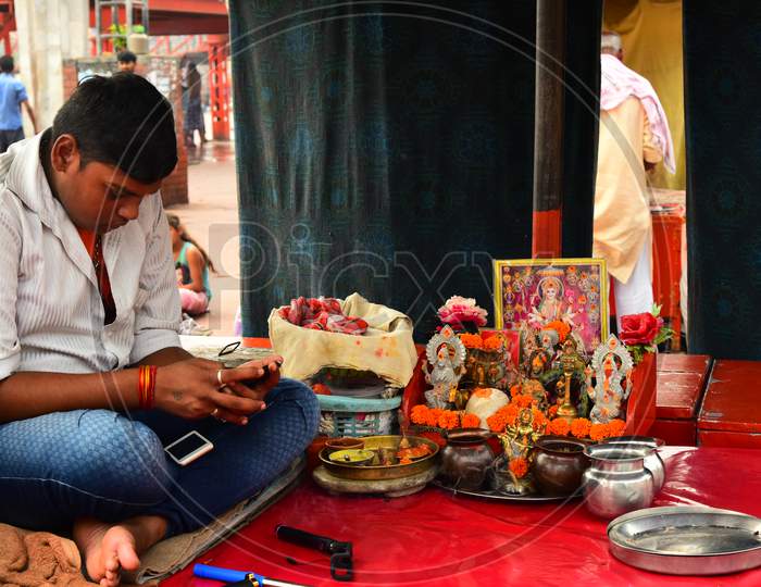 A Man Busily Checking His Smartphone By Sitting At a Small Pooja Place In Haridwar