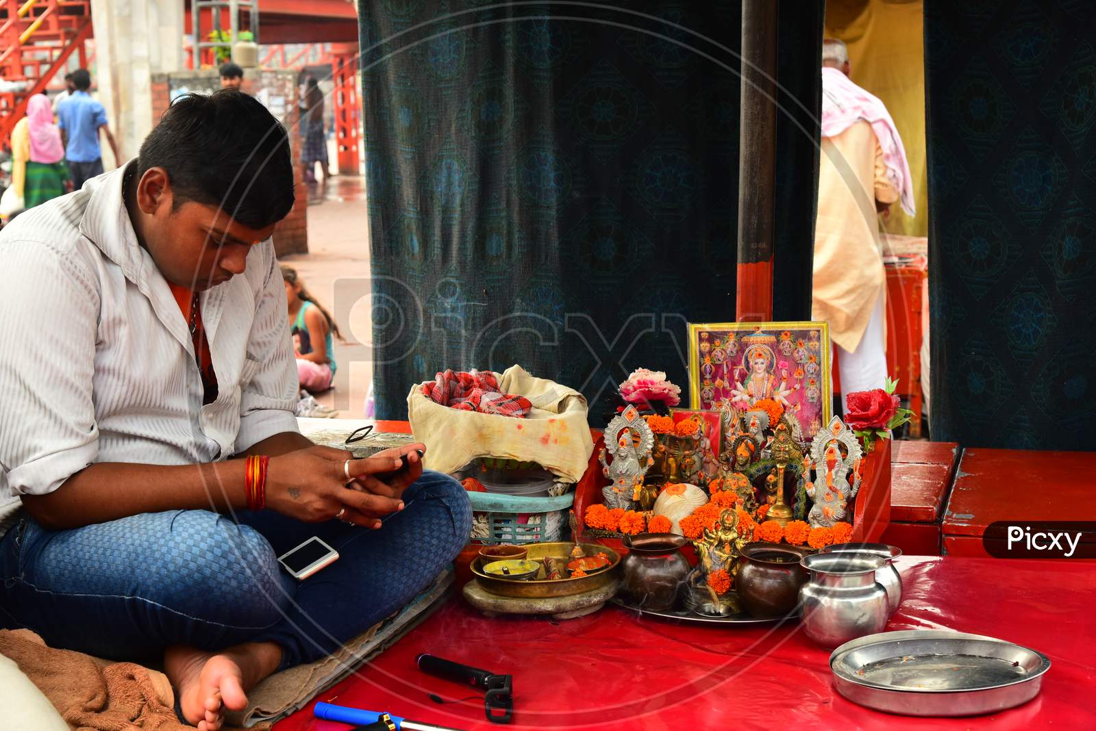 A Man Busily Checking His Smartphone By Sitting At a Small Pooja Place In Haridwar