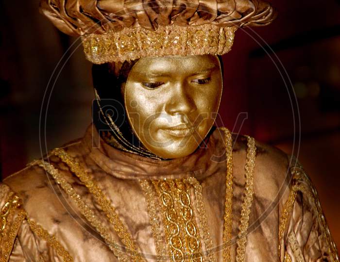 A Human Statue Artist Painted In Gold Colour