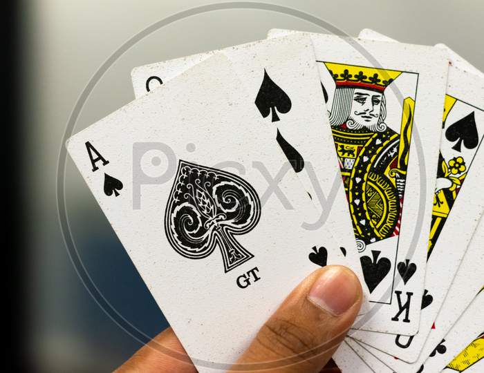 A hand holding ace, jack, queen, king of spades playing cards